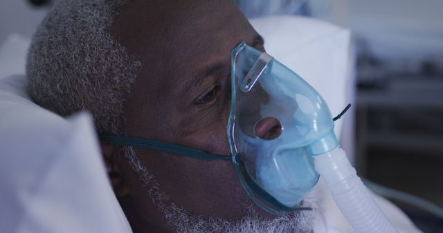 Senior man lying in hospital bed wearing oxygen mask, receiving respiratory treatment. Highlights importance of healthcare and medical attention for elderly patients. Useful for medical, healthcare, wellness, emergency services, and hospital-related content.