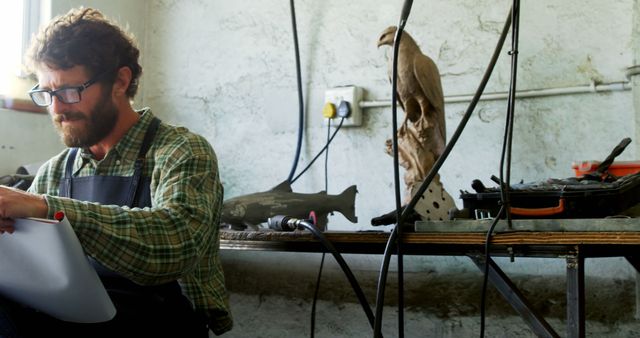 Male Artisan Reviewing Plans in Workshop with Measuring Tools and Bird Sculpture - Download Free Stock Images Pikwizard.com