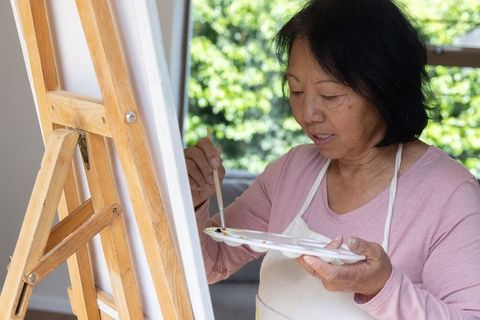 Senior Asian Woman Enjoying Home Painting Session with Canvas and Palette