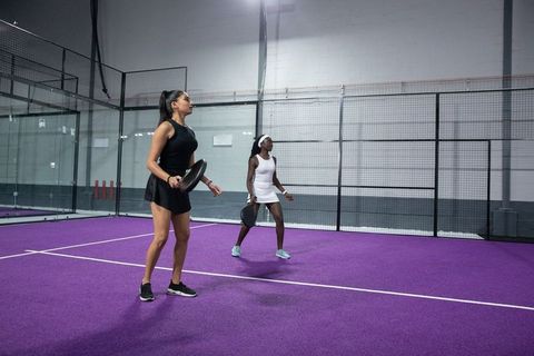 Indian and african american women playing padel on vibrant purple indoor court for fitness training