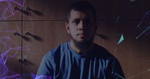 Moody low-key portrait of man sitting in blue athletic top with digital geometric overlays