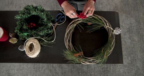 Creative hands garlanding grapevine wreath with pine and berries