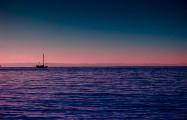 Boat peacefully floats on tranquil sea during twilight with pink and purple sky in the background reflecting on water. Ideal for themes related to tranquility, nature, maritime activities, sunset scenes and evening serenity. Great for websites, blogs, wallpapers, and motivational posters.