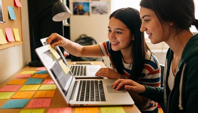 Two teen students collaborating on dorm desk with laptops and colorful sticky notes
