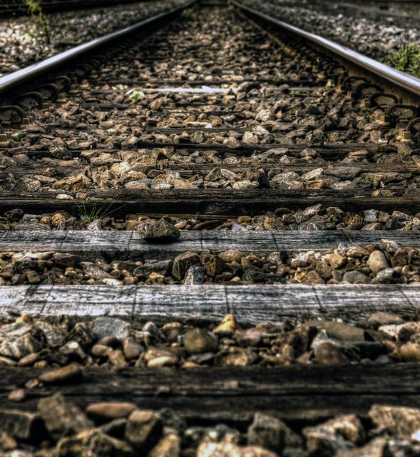 Detailed shot of old railroad track with wooden sleepers and gravel. Ideal for transportation, travel, or industrial themes, and can be used to depict journeys or paths. Suitable for backgrounds in presentations or brochures focusing on infrastructure, environment, or rustic settings.