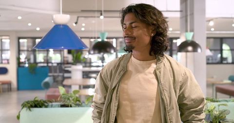 African american man standing in modern coworking lounge under colorful pendant lighting
