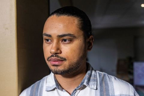 Thoughtful young man standing indoors near pillar wearing striped button-up shirt soft-lit