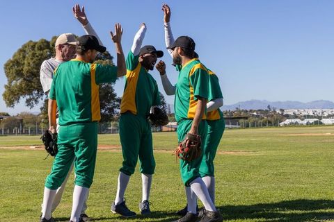 Baseball team celebrating on mound high-fiving after run wearing green uniforms