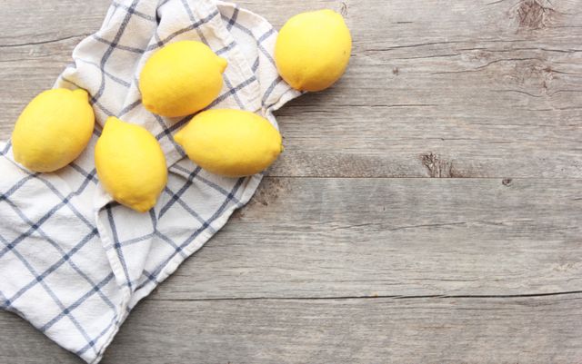 Fresh lemons placed on a checkered cloth spread out on a rustic wooden surface. Ideal for use in blogs, websites, and publications focused on cooking, healthy eating, and kitchen aesthetics. Perfect for social media posts and marketing materials focusing on organic products or citrus fruits. Conveys a fresh, clean, and vibrant appeal suitable for food photography and lifestyle themes.