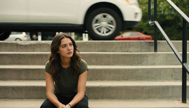 Pensive young woman sitting on concrete steps clasping hands with urban cars behind