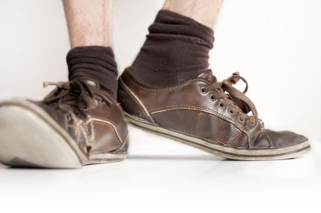 Close-up of worn leather shoes paired with brown socks on a white background. Useful for illustrating everyday casual footwear and vintage fashion themes. Perfect for lifestyle blogs, fashion articles, or advertisements focusing on urban style and comfortable clothing.