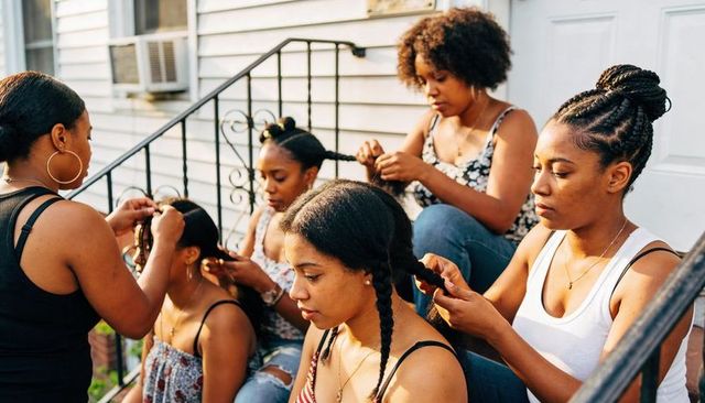 Women braiding hair on front steps during relaxed summer gathering