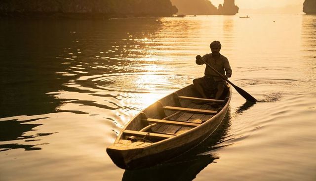 Sunset rowing boatman wearing headwrap and sarong on karst lagoon with golden reflection
