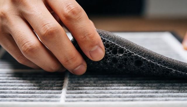 Hand peeling porous foam prefilter from pleated air filter during maintenance