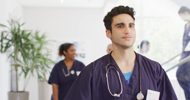 Image of smiling biracial male doctor walking in busy hospital corridor, with copy space - Download Free Stock Photos Pikwizard.com
