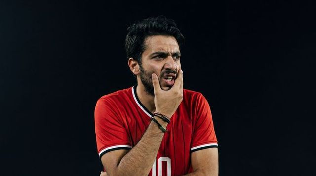 Indian athlete pressing jaw in red jersey 10 conveying tension and focus on dark backdrop
