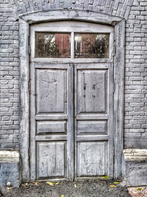 Vintage wooden door set in old brick building shows a weathered, rustic style. Perfect for editorials on history, architecture, cultural heritage, or artistic concepts related to time and decay. Suitable for use as background in design, historical renovations, or illustrative needs for aged and historic themes.