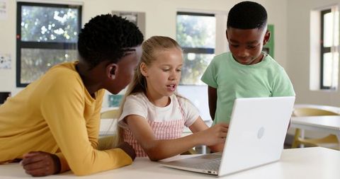 Diverse students collaborating on laptop in bright classroom sharing digital learning tools