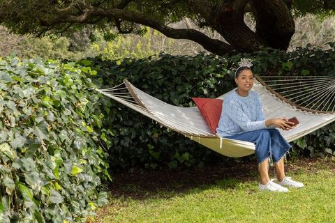 African american woman sitting on hammock in backyard holding smartphone wearing headband