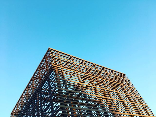 Modern architectural structure featuring a geometric steel framework against a clear blue sky. Can be used for themes related to architecture, modern design, construction, urban development, engineering marvels, contemporary buildings, or cityscape transformations.