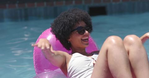 African american woman laughing and relaxing on pink float in sunny pool