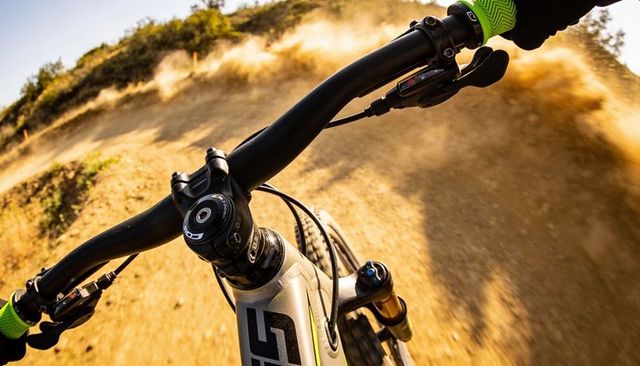 Riding mountain bike down dusty singletrack trail with bright green gloves at golden hour