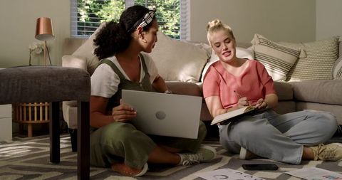 Two female students collaborating at home in cozy setting