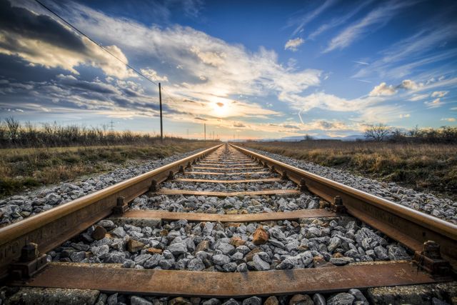 Capturing the beauty of a sunset over railway tracks with a dramatic sky filled with clouds, this photo emphasizes the perspective and freedom of the open horizon. Ideal for use in travel brochures, motivational posters, blog posts on adventure and exploration, and nature-themed websites.