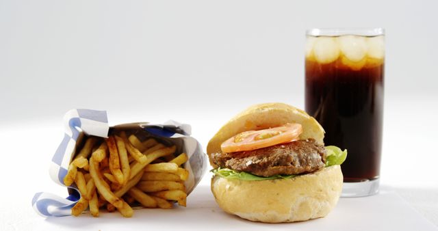Classic cheeseburger with tomato and lettuce served with a side of golden French fries in a paper container and a refreshing cola drink with ice cubes. Perfect for illustrating themes and concepts related to fast food, American cuisine, quick meals, comfort food, takeout, and casual dining. Ideal for use in restaurant menus, food delivery promotions, advertising campaigns, and culinary blogs.