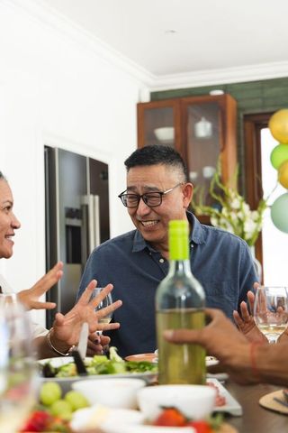 Family kitchen gathering with senior asian man enjoying wine and cheerful conversation