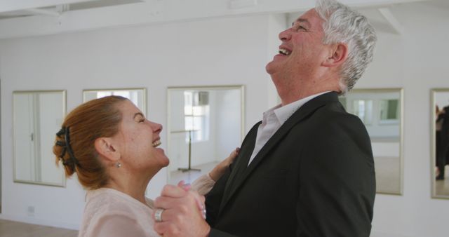Happy senior and mature caucasian couple dancing and laughing at ballroom dance class, copy space. Dance, hobbies, leisure, togetherness and active senior lifestyle, unaltered.
