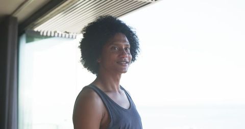 Standing man on coastal balcony wearing dark tank top gazing confidently at camera