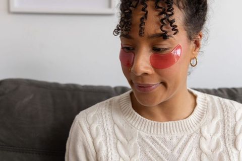 African american woman relaxing with red hydrogel eye patches on sofa skincare routine