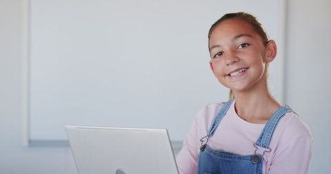 Smiling Young Girl Using Laptop in Classroom with Whiteboard
