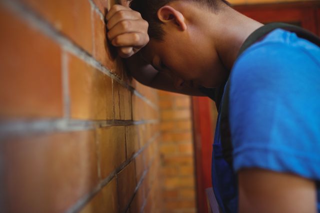 Sad schoolboy leaning on brick wall in school