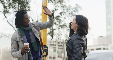 African American man and woman giving high five at urban crosswalk holding coffee, smiling