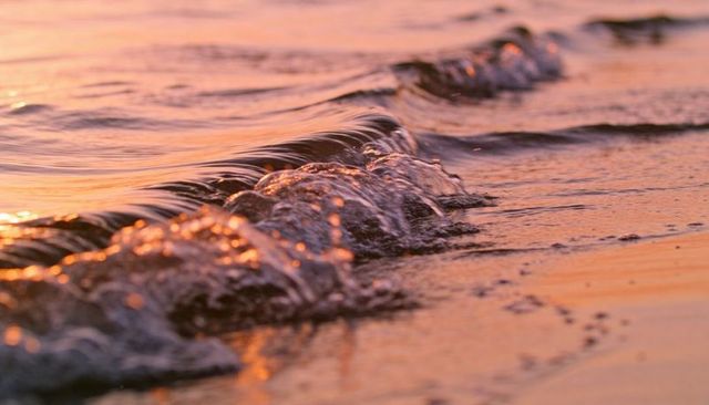 Breaking small waves rolling onto wet sand at sunset reflecting warm golden light