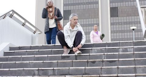 Mature diverse women tying sneakers on urban steps preparing for outdoor yoga session