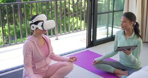 Diverse female coach guiding virtual reality meditation participant on balcony at home