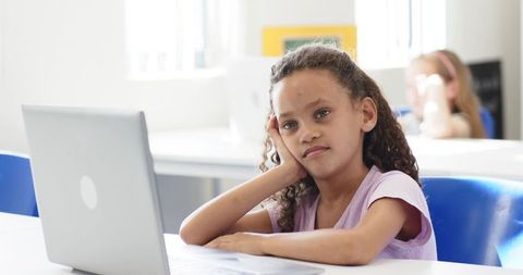 Schoolgirl using laptop looking thoughtful during classroom learning session