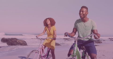 Joyful couple riding bicycles along sandy beach at sunset