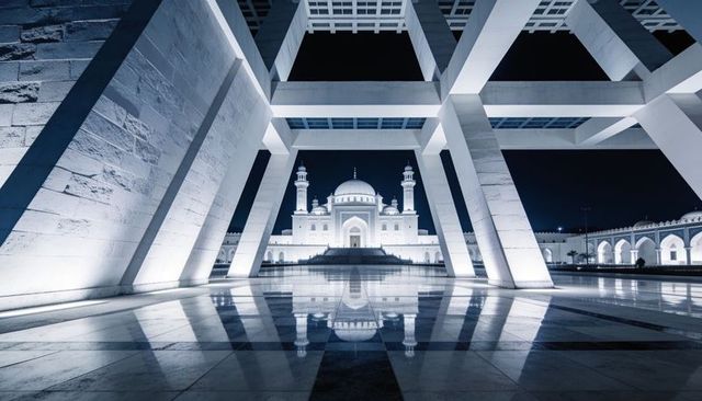 Nighttime symmetrical mosque framed by modern concrete grid with reflective marble plaza
