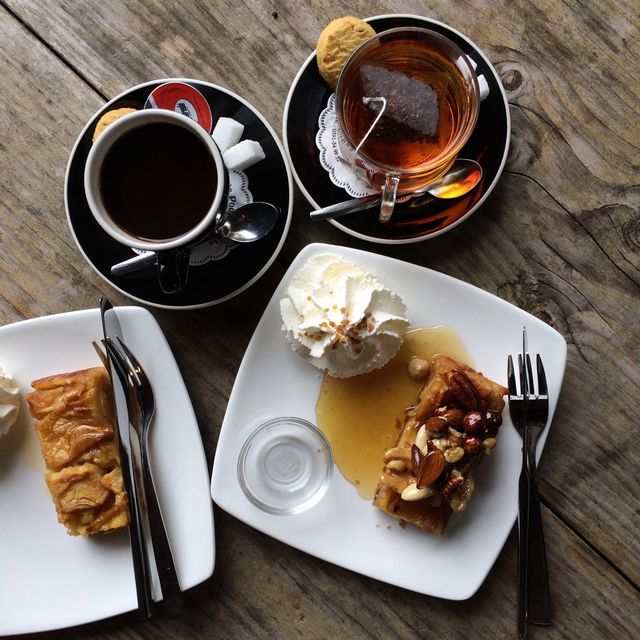 Pastries served with coffee and tea on a wooden table. Image showcases pleasant arrangement of delicious desserts alongside black coffee and tea, each with whipped cream and nuts. Available in everyday or special occasion dining settings. Great for use in food blogs, cafe advertisements, menu designs, and social media promoting cozy and inviting cafe atmospheres.
