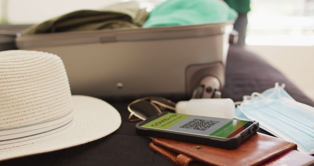 Scene shows travel essentials on bed, including suitcase, face mask, smartphone with COVID-19 vaccination proof, hat, and other items. Perfect for depicting travel preparation, safety precautions during travel, or packing for a vacation or business trip.