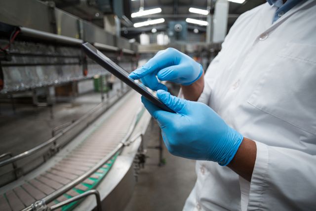 Factory engineer using digital tablet in drinks production plant, wearing blue gloves and white coat. Ideal for illustrating modern manufacturing processes, quality control, industrial automation, and technology in the beverage industry.