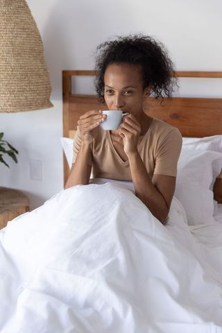 African american woman sipping morning coffee in minimalist white bedroom