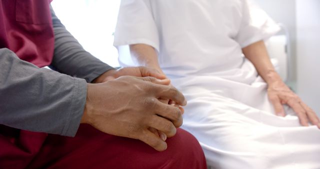 Midsection of diverse doctor and patient sitting on bed holding hands in hospital room - Download Free Stock Photos Pikwizard.com