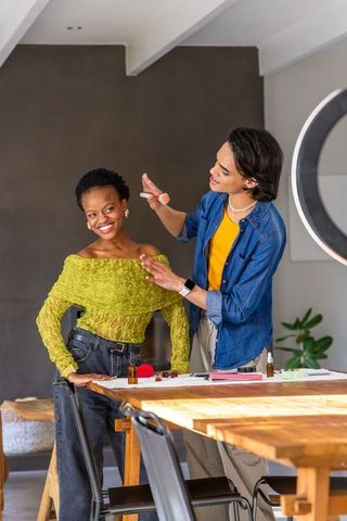 Makeup artist applying natural glam on smiling model at cozy home dining table beauty guide