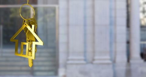 Golden House-Shaped Keys Hanging in Front of Building Background