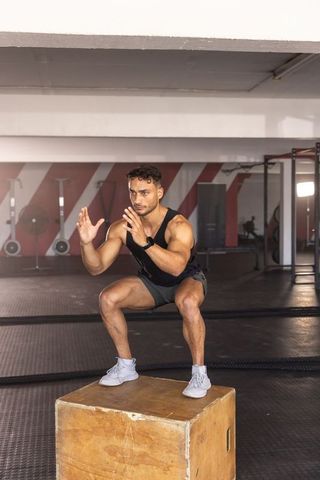 Male athlete performing box squat on plyometric box in gym for explosive leg power